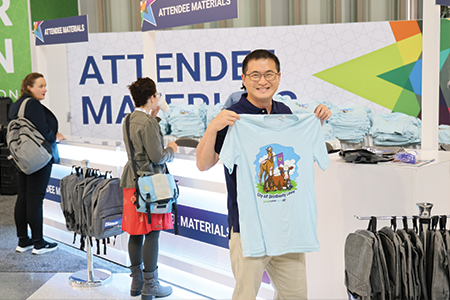 Man smiling holding up blue shirt in front of materials desk.
