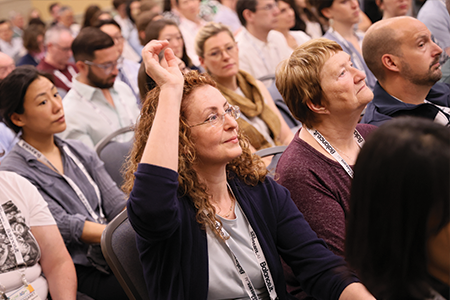 Woman sitting with other attendees and raising her hand.