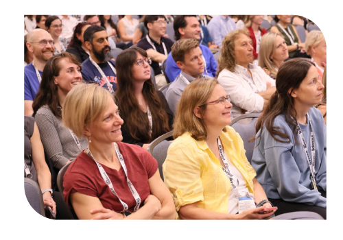 A group of attendees smiling at a speaker out of frame during a session.