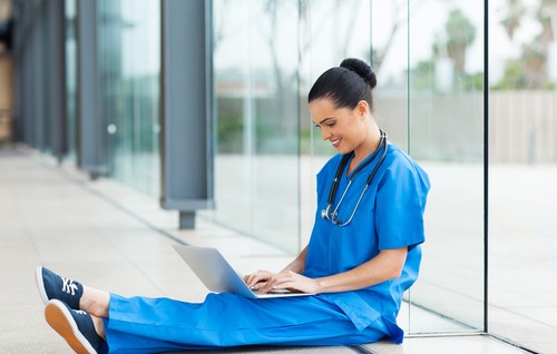 Woman in scrubs sitting on floor looking at laptop
