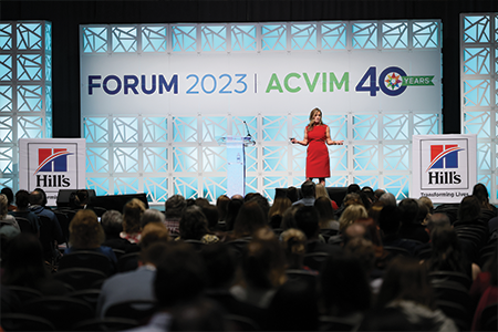 Speaker in red dress on stage in front of crowd.