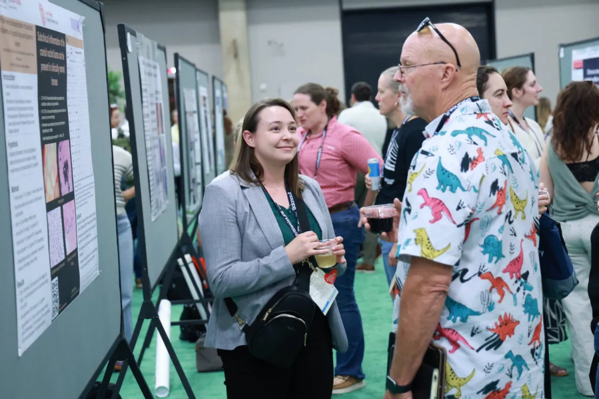 Two people stand in front of a research abstract poster during the ACVIM Forum
