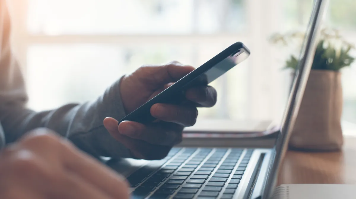 A person holds their cellphone while their laptop is open 