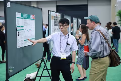 Person pointing to poster and talking and another attendee in poster park